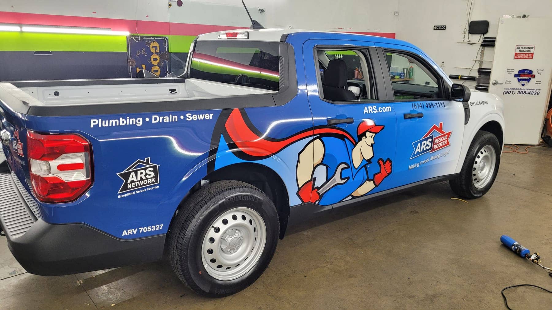 Blue Ford Maverick pickup with ARS Rescue Rooter cartoon-plumber graphics on the bed side
