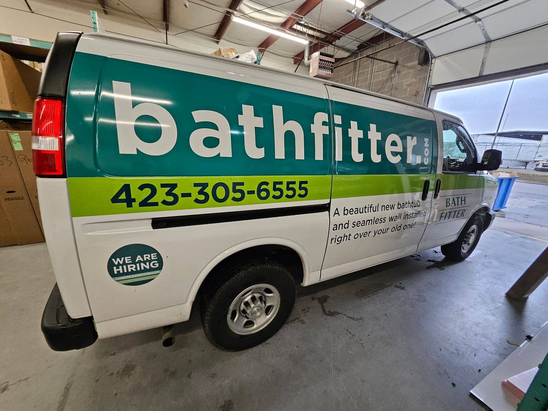 Chevy Express van in a green and white Bath Fitter wrap with hiring message on the rear