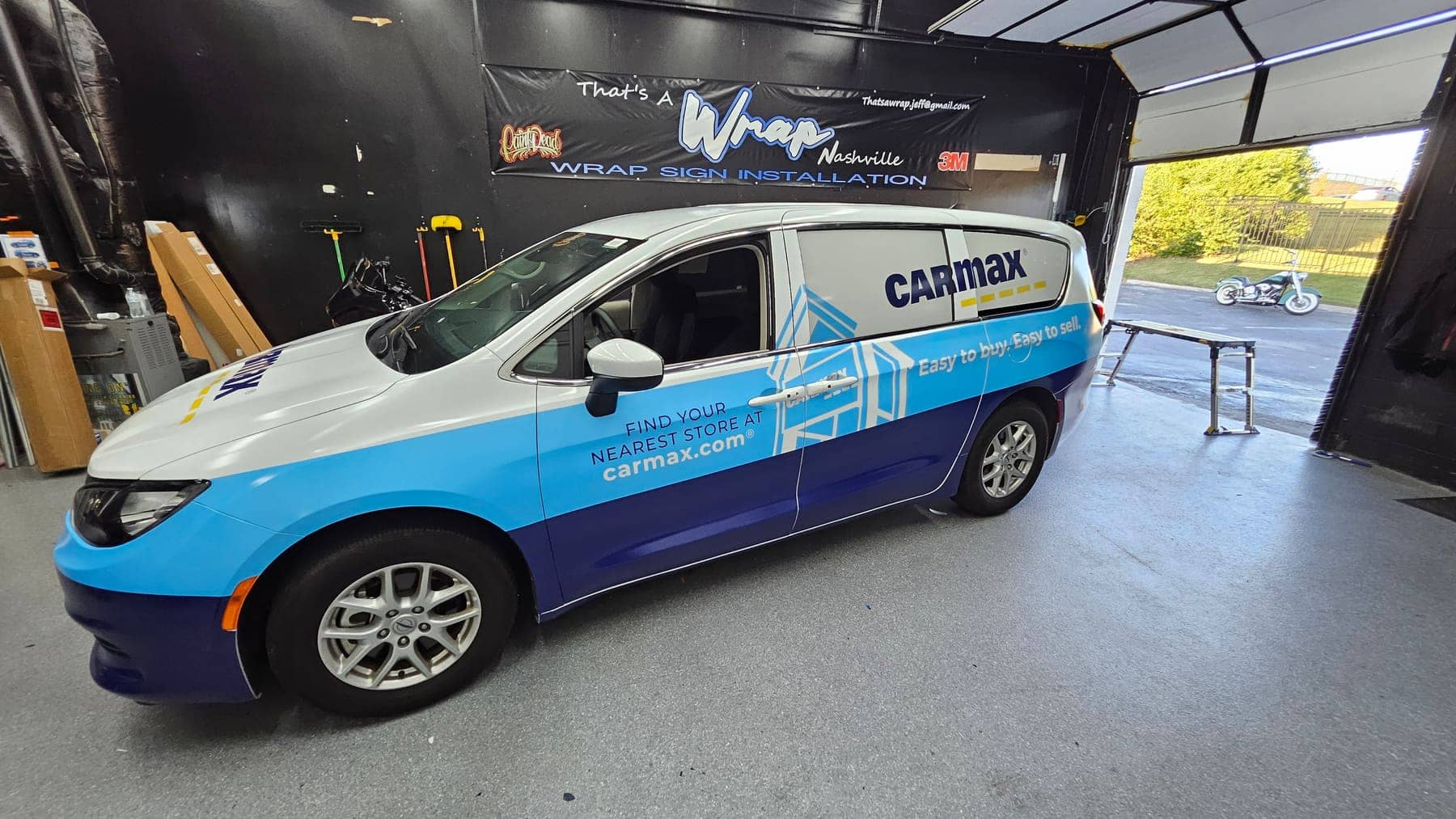 Chrysler Pacifica minivan in a two-tone blue CarMax wrap inside the wrap bay