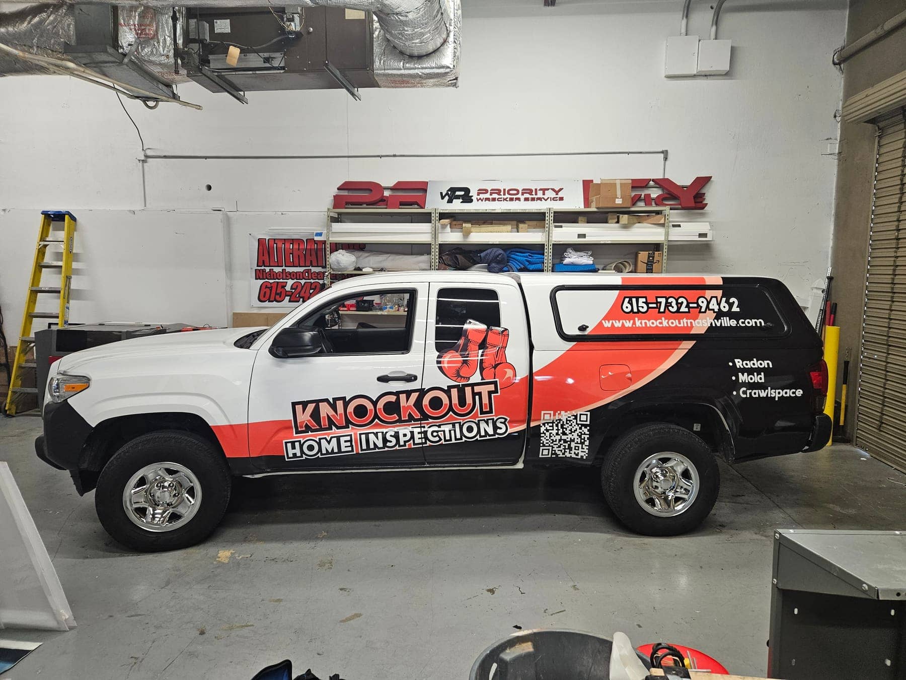 Toyota Tacoma with black, white, and red Knockout Home Inspections partial wrap in the shop