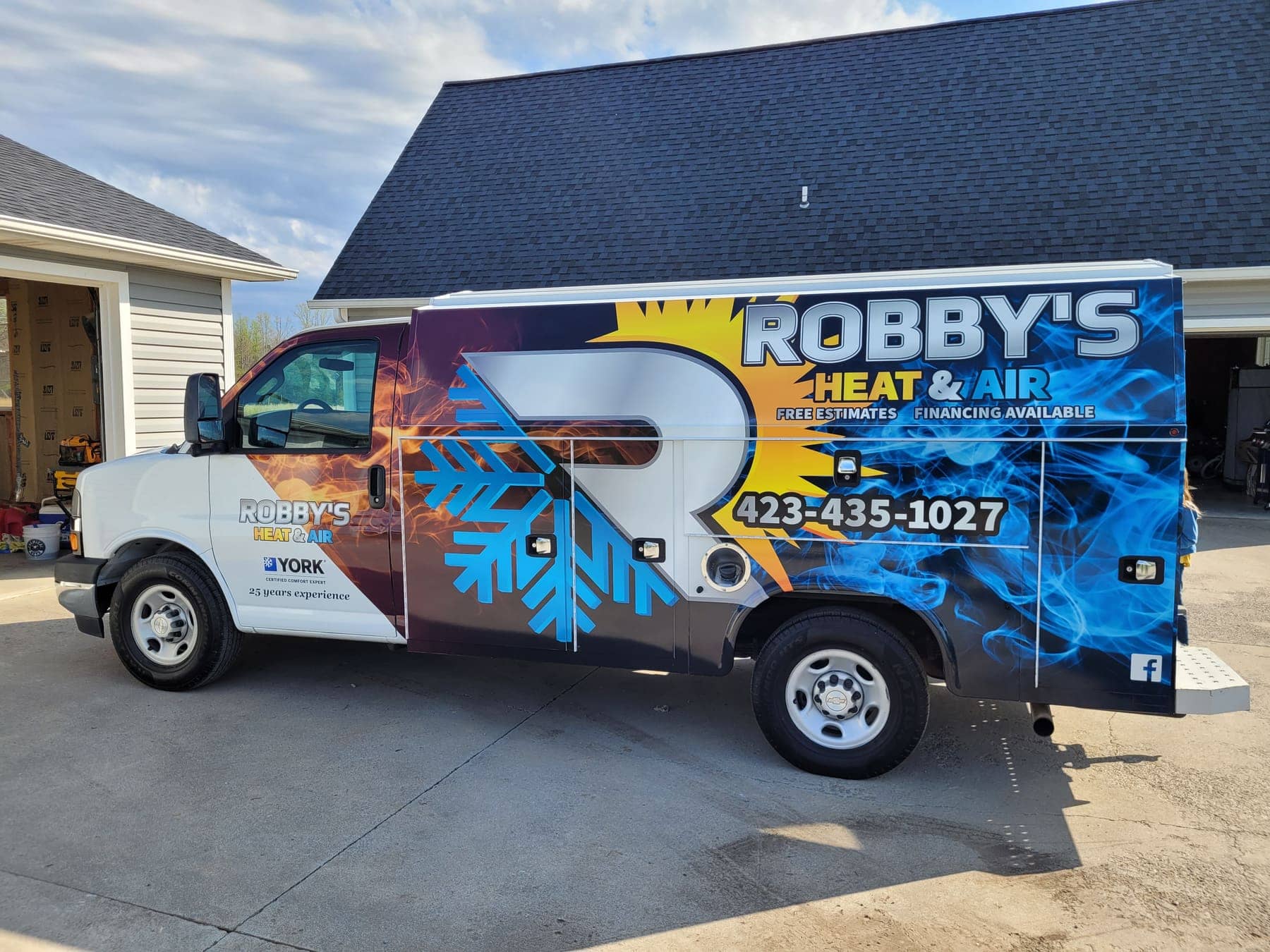 Utility van in a blue flame-themed full wrap for Robby's Heat and Air, parked outside the shop