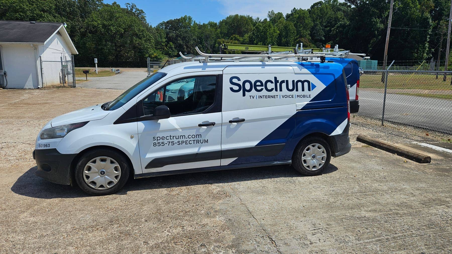 White Ford Transit Connect with blue Spectrum fleet graphics parked on gravel