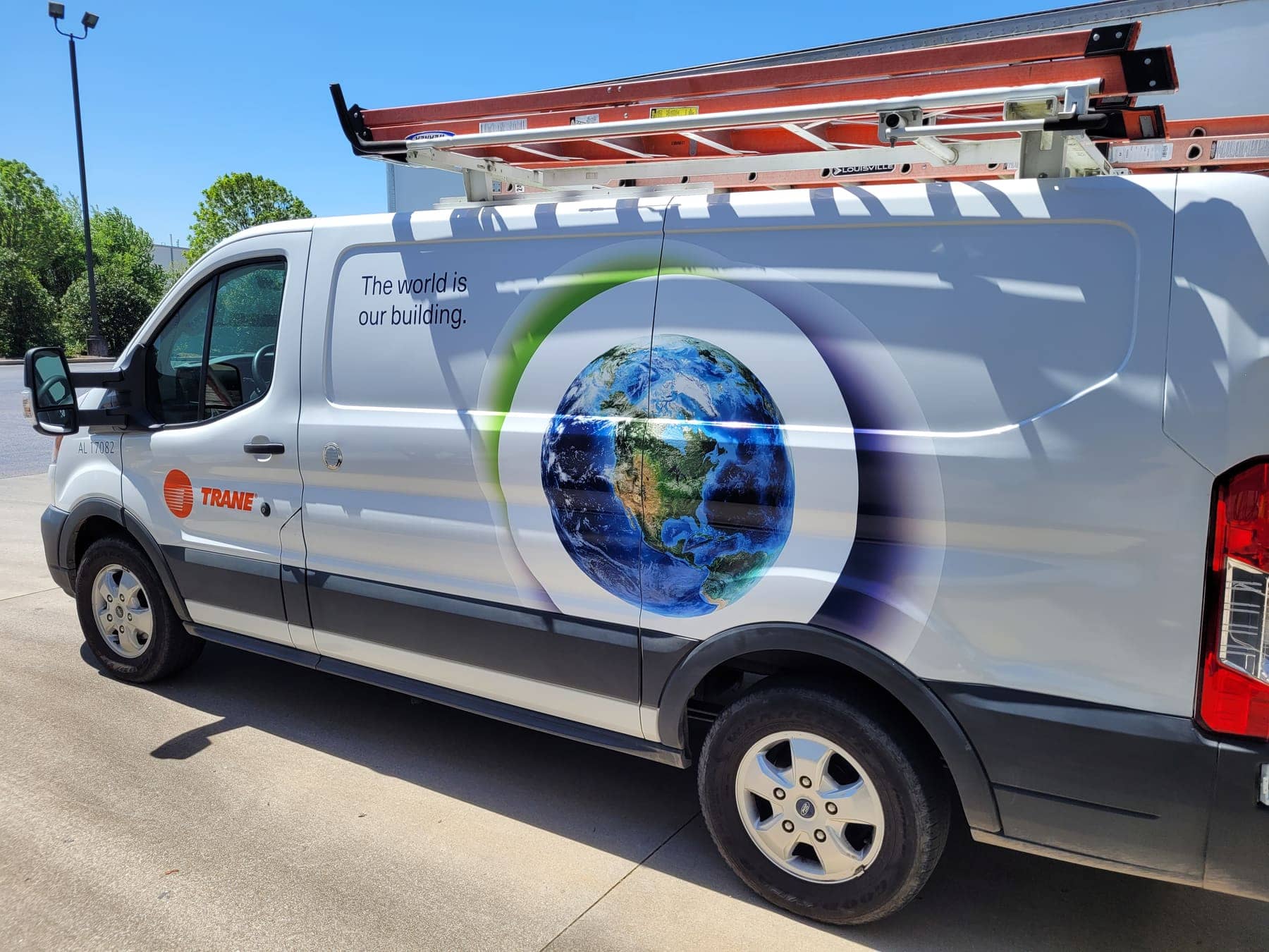 White Ford Transit with a globe-and-leaf Trane graphic wrapping the rear quarter