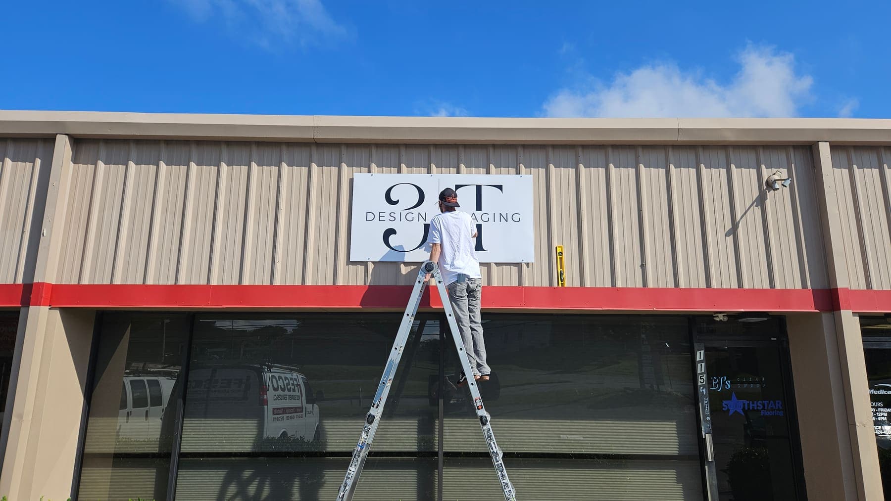 Installer on a ladder mounting a storefront sign panel