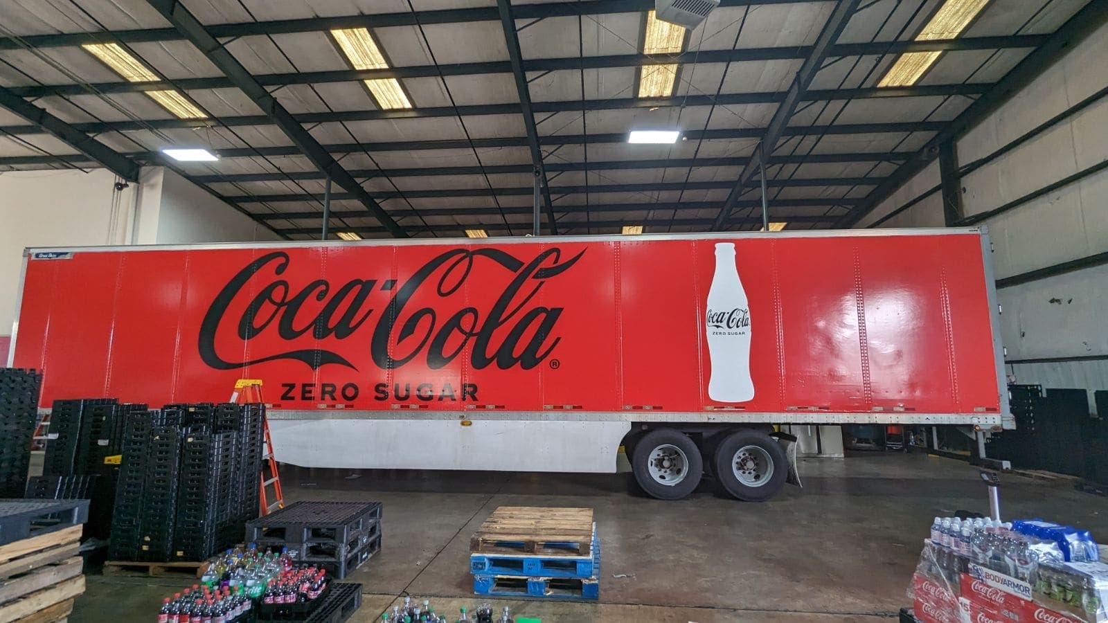 Red Coca-Cola Zero Sugar semi-trailer wrap with a giant contour bottle, inside a warehouse