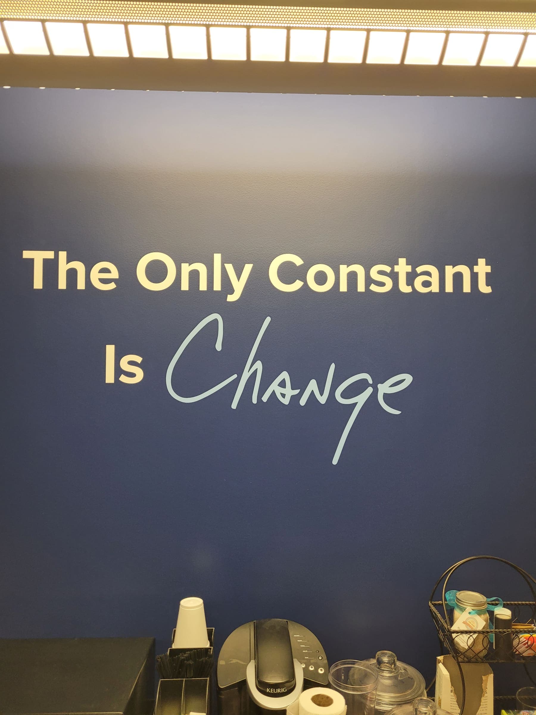 Gold cut-vinyl wall quote reading The Only Constant Is Change on a navy office wall