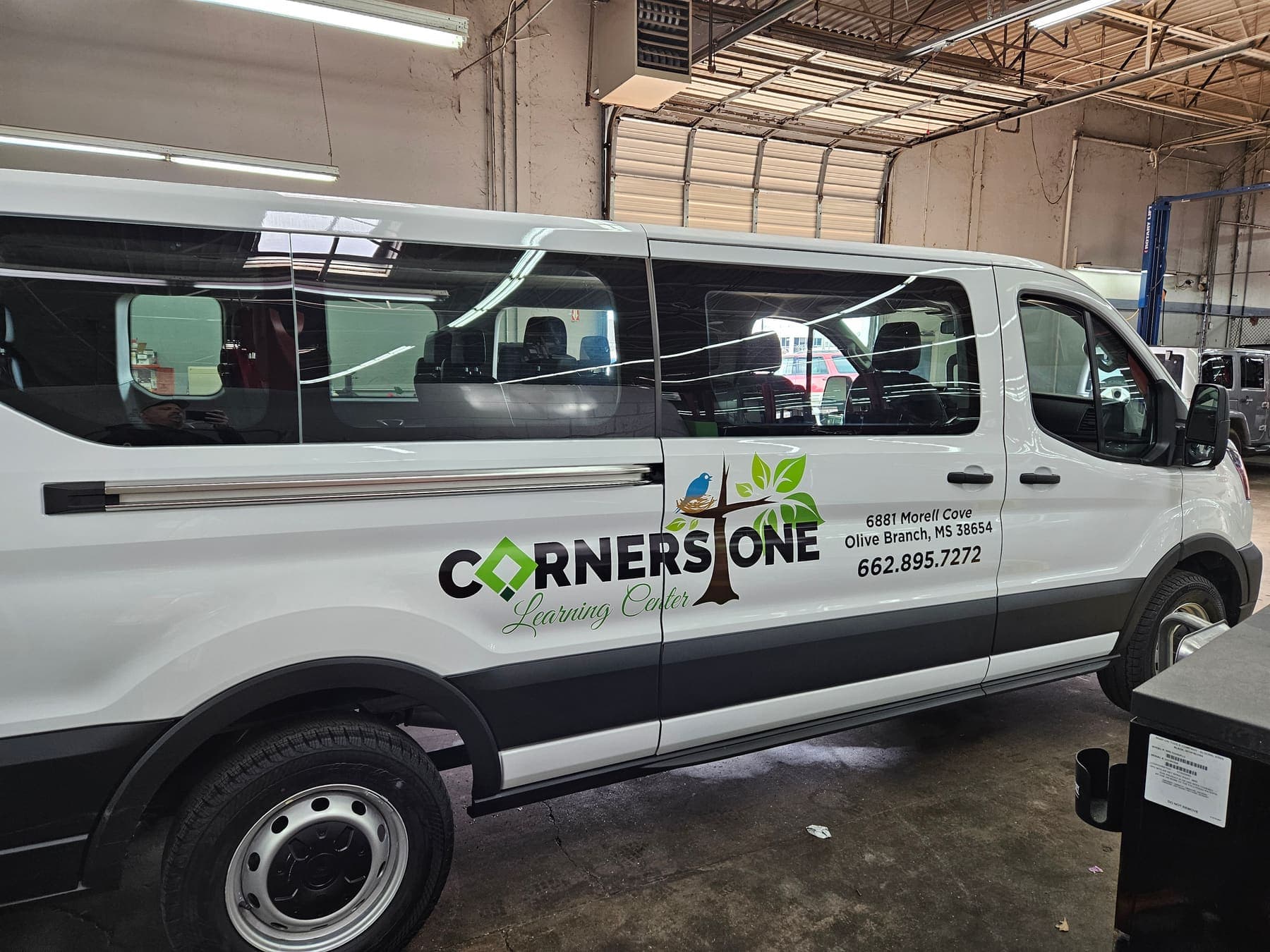 White Ford Transit passenger van with green Cornerstone Learning Center door lettering