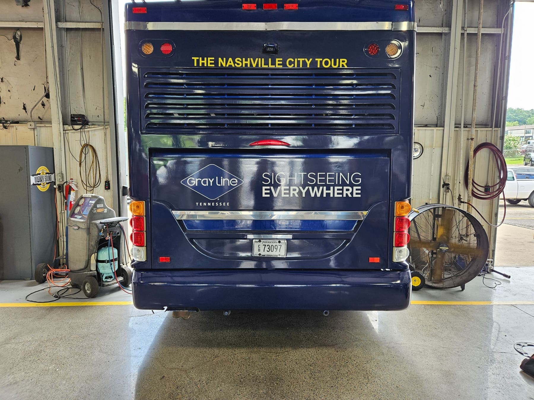 Rear of a single-deck Gray Line tour bus in navy with white script lettering, inside the garage