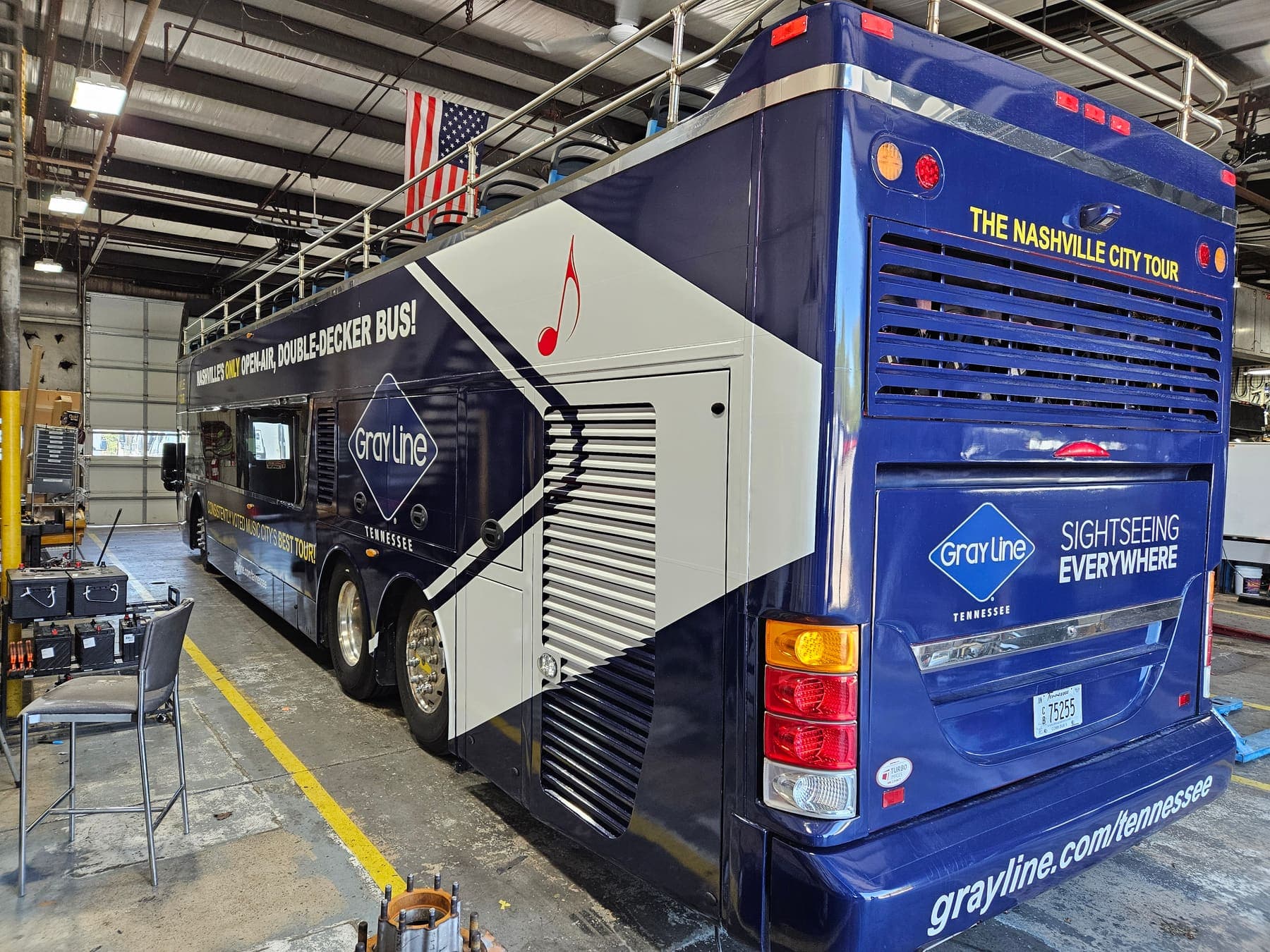 Rear of the double-decker showing wrapped engine panels, ladder, and music-note graphics