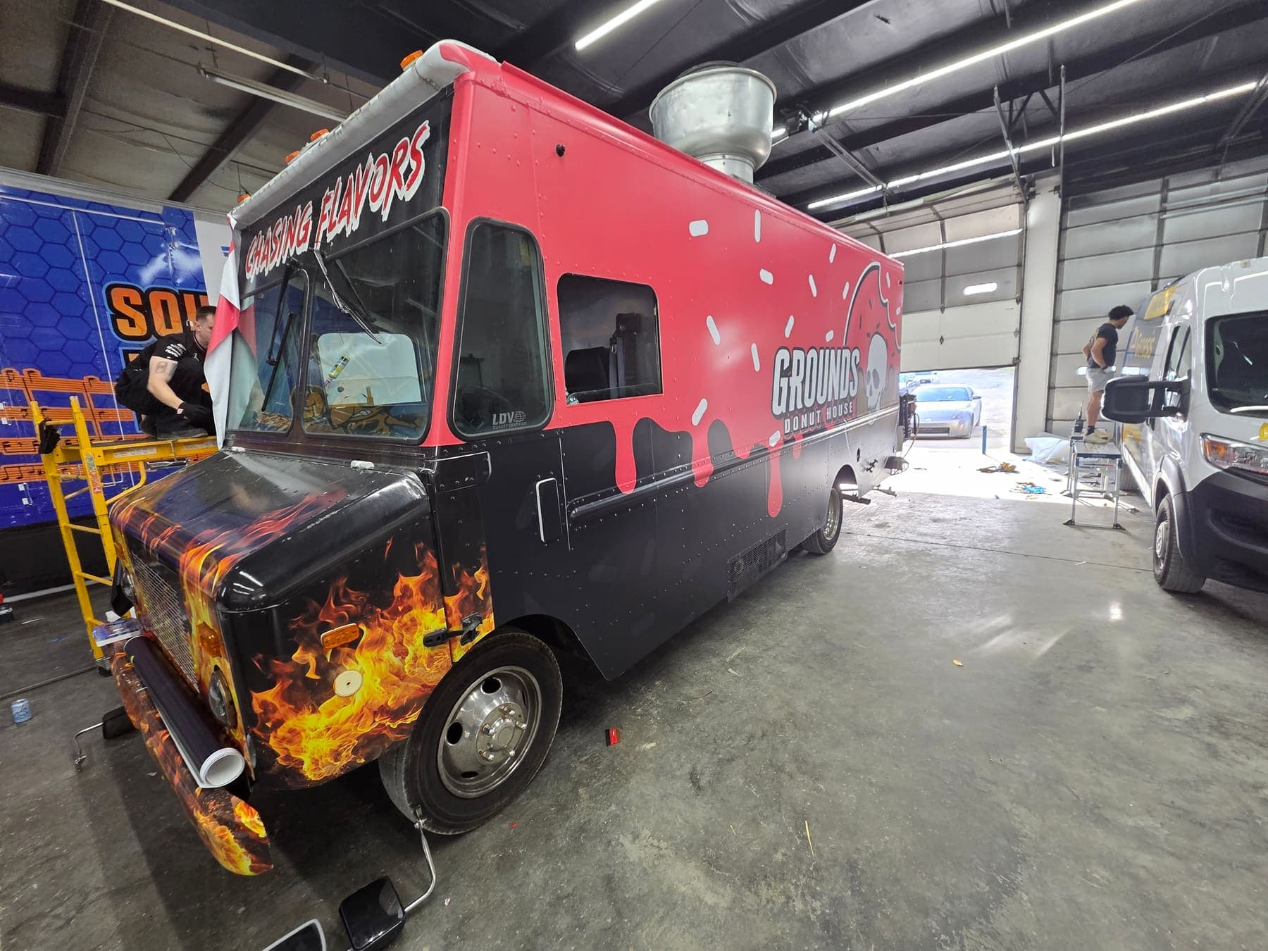 Red and black donut food truck with airbrush-style flames along the hood, inside the shop
