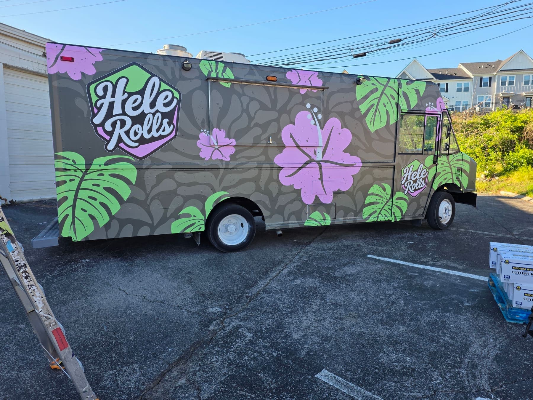 Hele Rolls food truck wrapped with tropical monstera leaves and hibiscus over a charcoal base