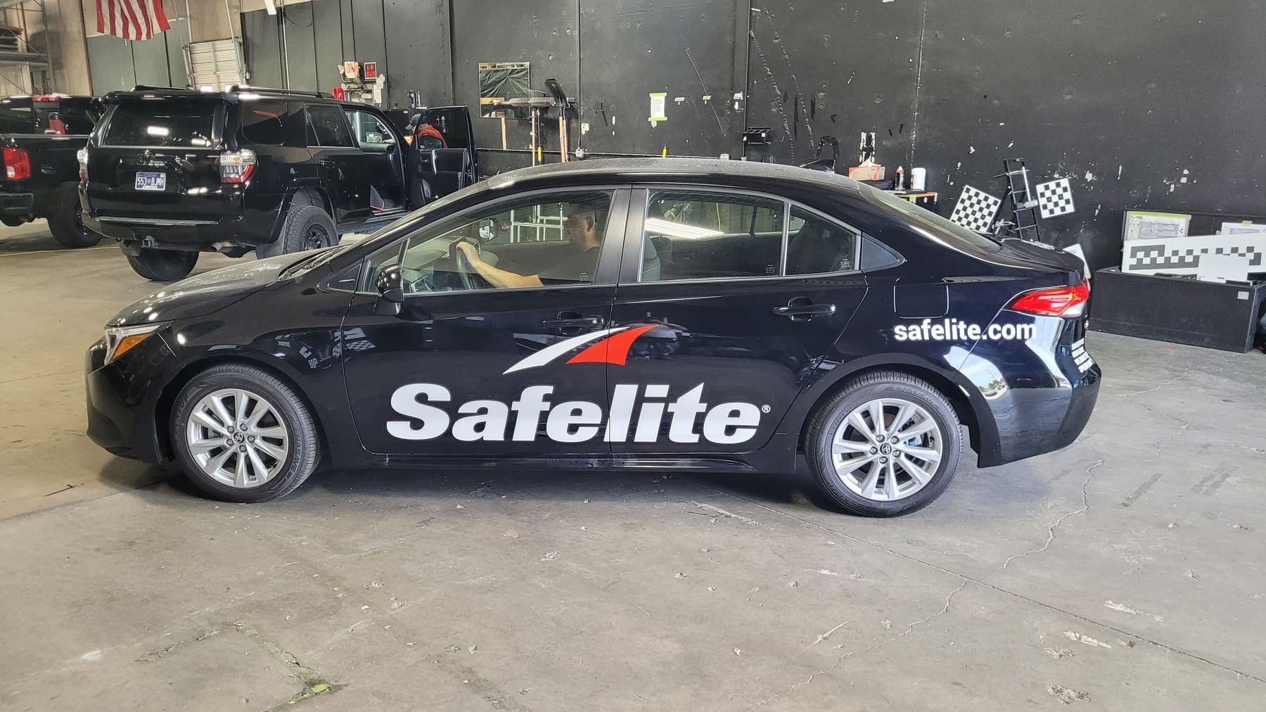 Black Toyota Corolla with white Safelite lettering and red logo accents in the shop